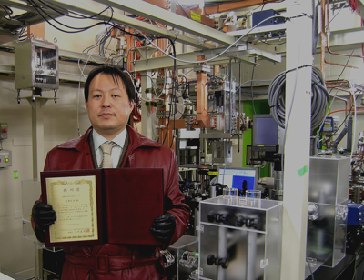 Dr. Hiromitsu Tomizawa in front of verification test equipment for the z-polarized photocathode electron guns he developed