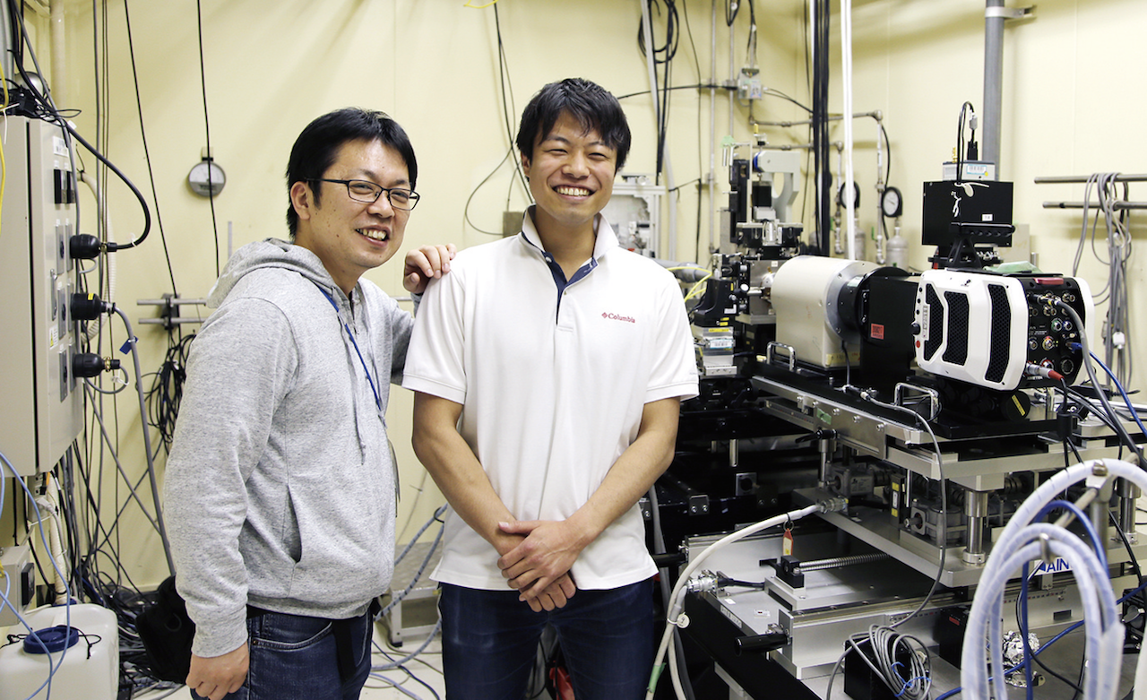 SPring-8 BL40XU内にて先輩（左：高輝度光科学研究センター関口さん）と“はにかむ”佐々木さん（右）