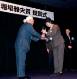 堀場雅夫最高顧問から表彰を受け取る寺田研究員(写真右側)。