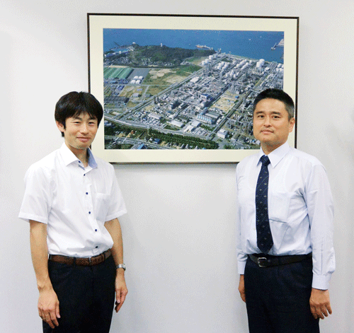 エラストマーを製造している工場写真を前に、高柳さん（左）と本田さん（右）